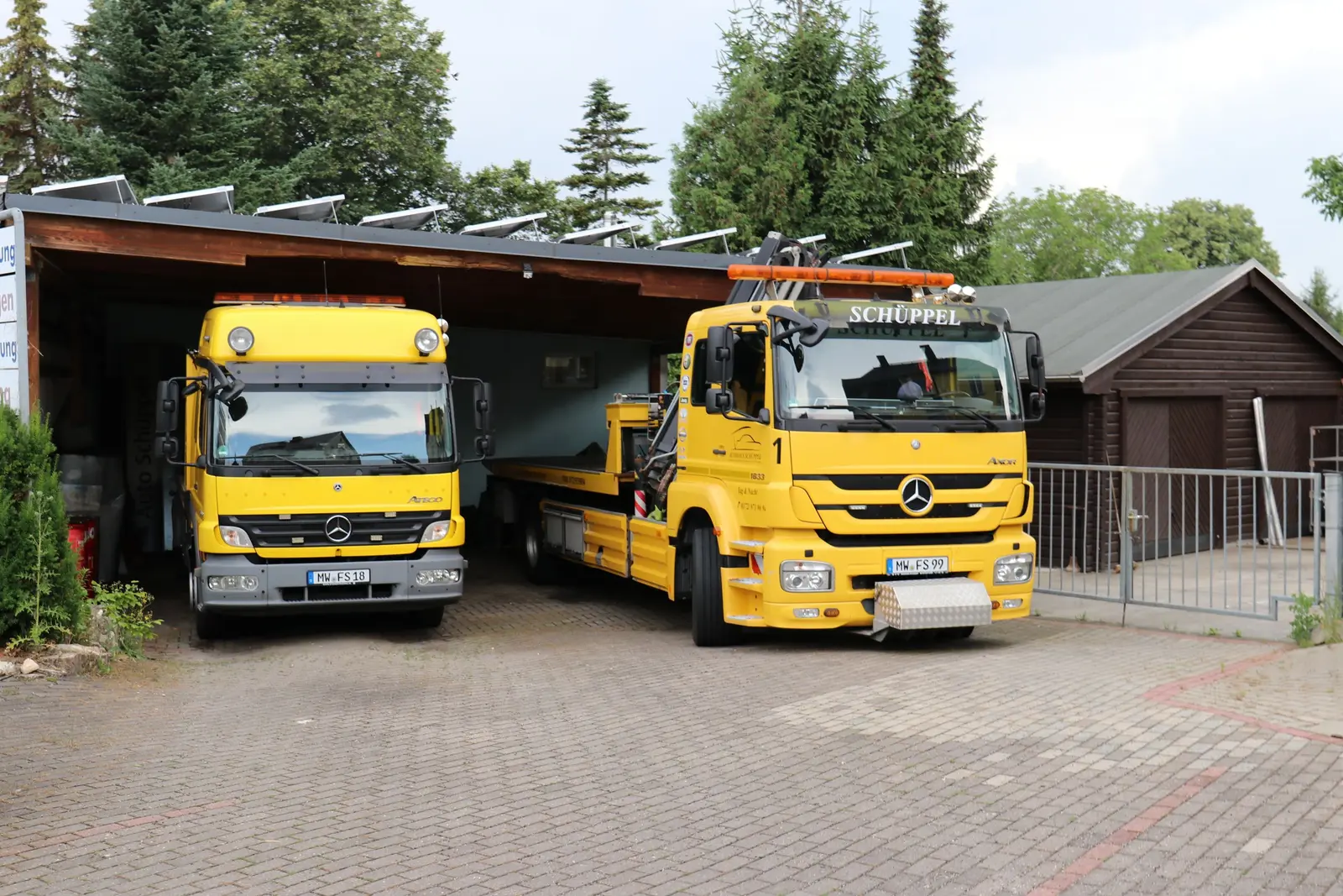 Zwei gelbe Abschleppwagen von Autohaus Schüppel vor der Fahrzeughalle